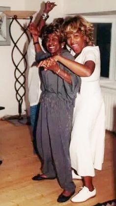 two women are dancing together in the living room with their arms around each other and smiling