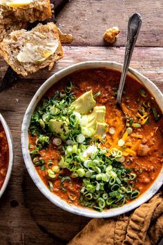 two bowls of chili soup with bread and avocado garnish on the side