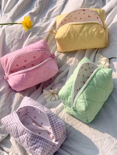 four small purses sitting on top of a bed next to a yellow and white flower