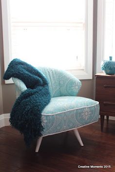 a blue chair sitting in front of a window with a blanket on it's back