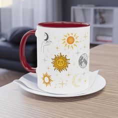 a red and white coffee mug sitting on top of a table next to a plate