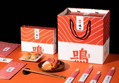 an orange table topped with sushi and chopsticks next to a box of food