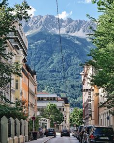 cars parked on the side of a road in front of tall buildings with mountains in the background