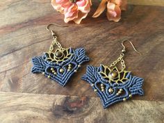 a pair of blue and gold earrings sitting on top of a wooden table next to flowers