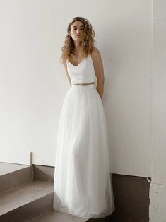 a woman in a white dress leaning against a wall with her hands on her hips