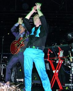 two men are performing on stage with their hands in the air and one is holding his guitar