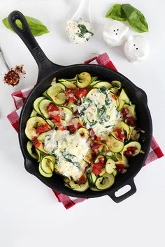 a skillet filled with zucchini, tomatoes and spinach on top of a red checkered cloth