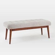 an upholstered bench with wooden legs and a buttoned seat pad on the back