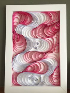 an abstract paper art piece with pink and white swirls on the bottom, in a white frame