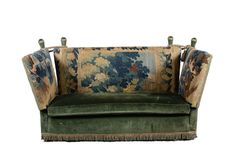 an upholstered green velvet sofa with floral tapestry on the back and tassels