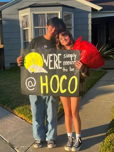 two people standing in front of a house holding a sign that says we're simply meant to be hoco