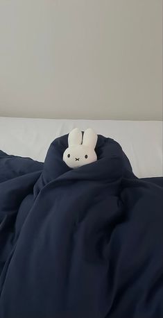 a white stuffed animal sitting on top of a blue comforter covered in a blanket