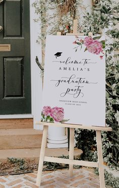 a white sign with pink flowers on it sitting in front of a door that says welcome to america's graduation party