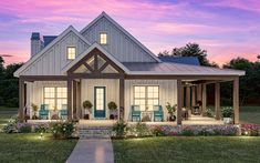 a white house with blue chairs on the front porch at dusk, surrounded by flowers and greenery