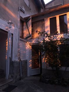 the sun is shining down on an old building with shutters and trees in front of it