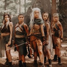 a group of women standing next to each other in front of a forest with trees