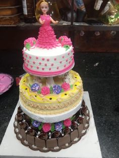 a three tiered cake with a barbie doll on top and other cakes in the background