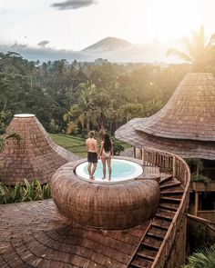 two people are standing on the edge of a hot tub in front of some thatched huts