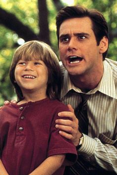 a man holding a young boy who is wearing a shirt and tie with his mouth open