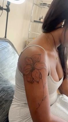 a woman with a flower tattoo on her arm and shoulder, sitting in front of a bed