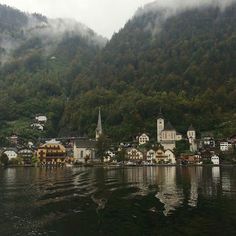 a small town on the shore of a lake surrounded by mountains and foggy clouds