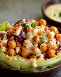 a bowl filled with lettuce and chickpeas covered in dressing next to another bowl