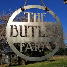 a metal sign that says the butler farm hanging from a chain in front of some trees