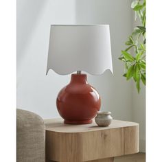 a table lamp with a red vase on it and a white shade over the base