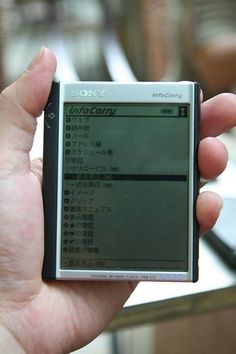 a hand holding a small electronic device in it's left hand, with japanese writing on the screen