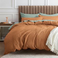 a bed with orange and green comforters in a white room next to a brown headboard