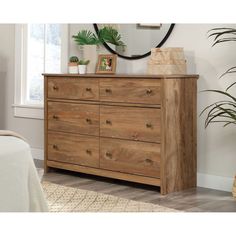 a wooden dresser sitting in front of a window next to a potted plant on top of a rug