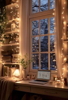 a laptop computer sitting on top of a desk next to a window covered in fairy lights