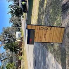 a wooden sign sitting on the side of a road next to a field and trees