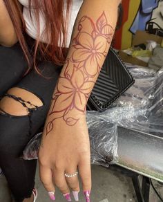 a woman with pink nails is sitting on a bench and has a flower tattoo on her arm