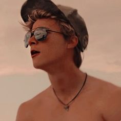 a shirtless man wearing sunglasses and a hat on top of his head is looking off to the side