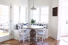 a dining room table with four chairs and a bench in front of two windows that look out onto the backyard