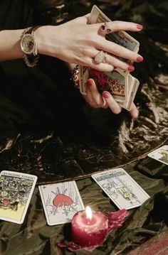 a woman's hands holding playing cards next to a candle and tarot cards