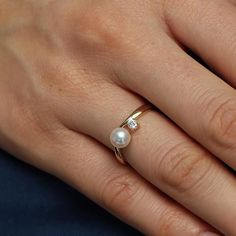 a woman's hand with a pearl and diamond ring on her left hand, wearing a yellow gold band