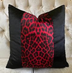 a red and black pillow on top of a white couch with a leopard print design