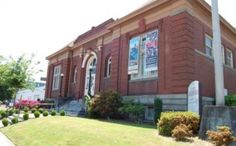 an old red brick building with a sign in front of it on the grass and trees