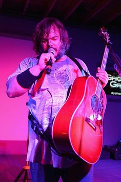 a man holding a guitar and singing into a microphone while standing in front of a stage