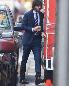 a man in a blue suit and tie standing next to a car on the street