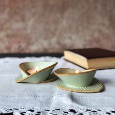 two tea cups and saucers sitting on top of a table next to a book