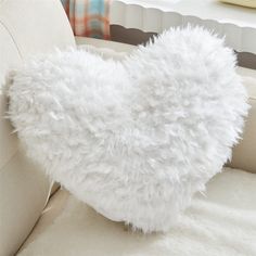 a fluffy white heart shaped pillow sitting on top of a couch next to a window