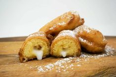 powdered sugar covered doughnuts sit on a cutting board