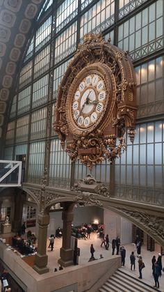 a large clock hanging from the side of a building next to people walking around it