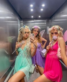 three beautiful women dressed in fairy costumes standing on an escalator and taking pictures with their cell phones