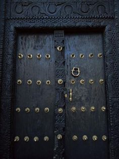 an ornate black door with gold knobs and rings on the front part of it