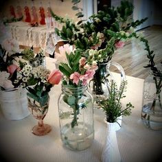 four vases with flowers and greenery in them sitting on a white table cloth