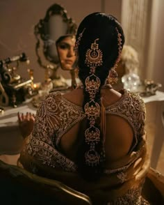 a woman sitting in front of a mirror with her back turned to the camera, wearing an intricately designed headpiece